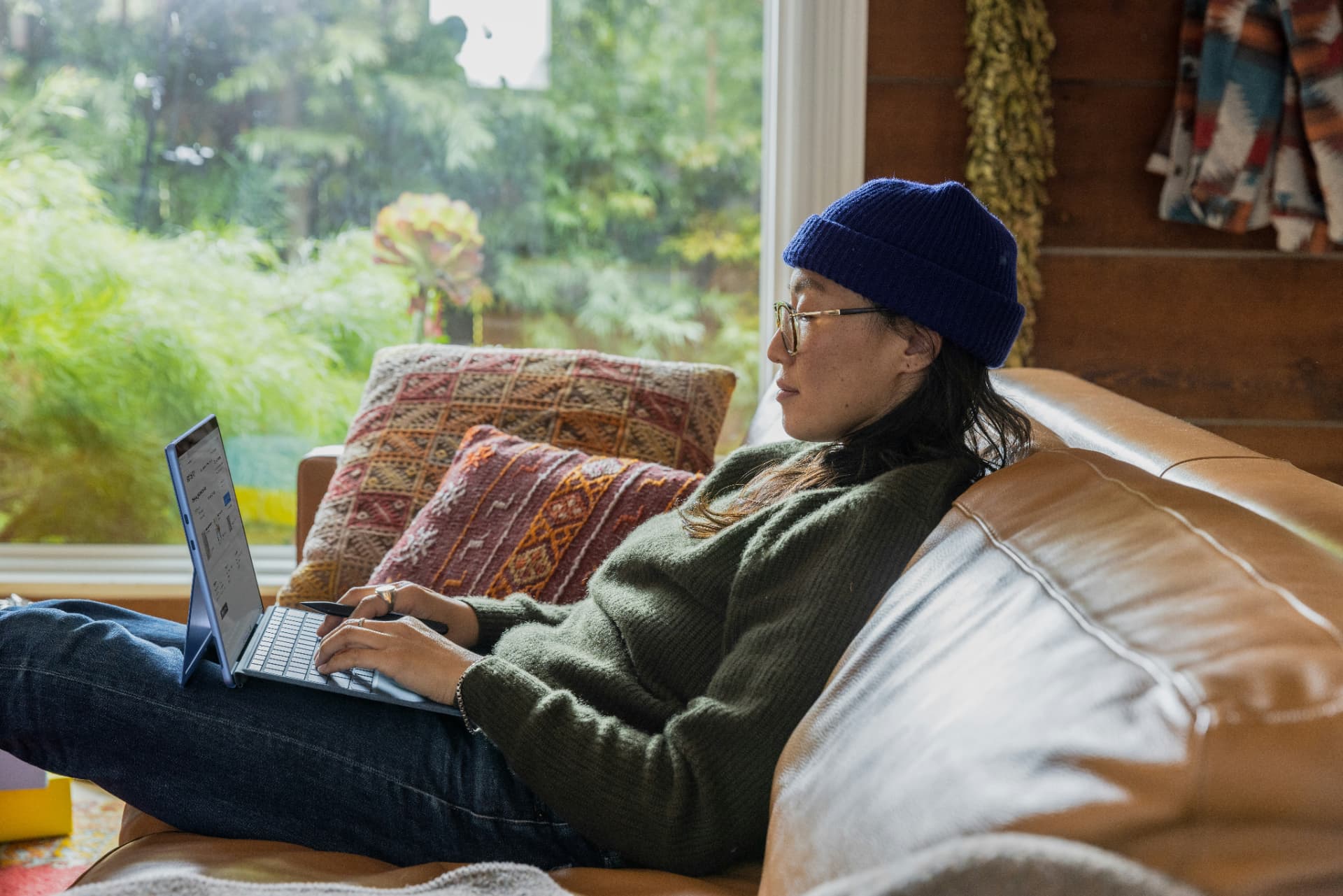 A person reading on a tablet at home beside a garden window